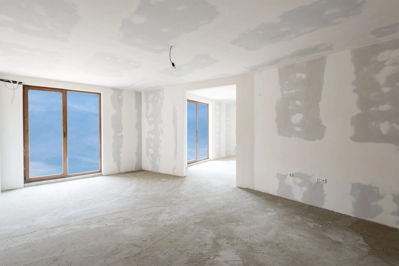 Pièce avec murs préparés pour la peinture, montrant des surfaces enduites et lissées avec fenêtres encadrées en bois.